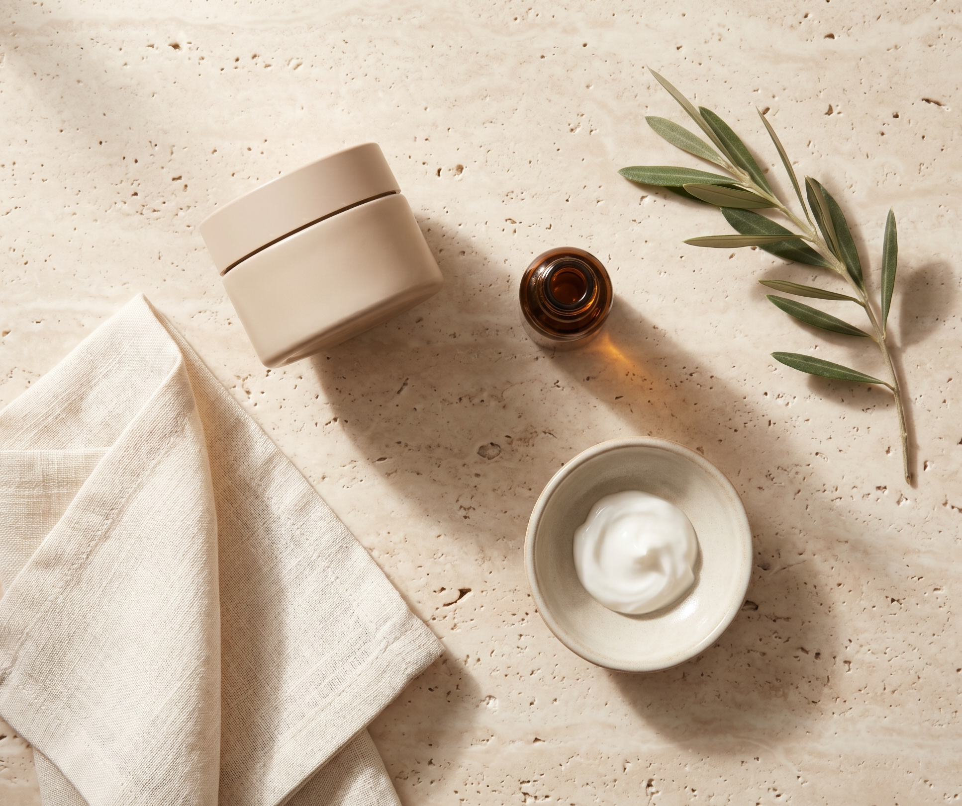 http://Crema%20hidratante,%20sérum%20y%20rama%20de%20olivo%20sobre%20mesa%20de%20mármol%20travertino%20en%20composición%20editorial%20cálida.